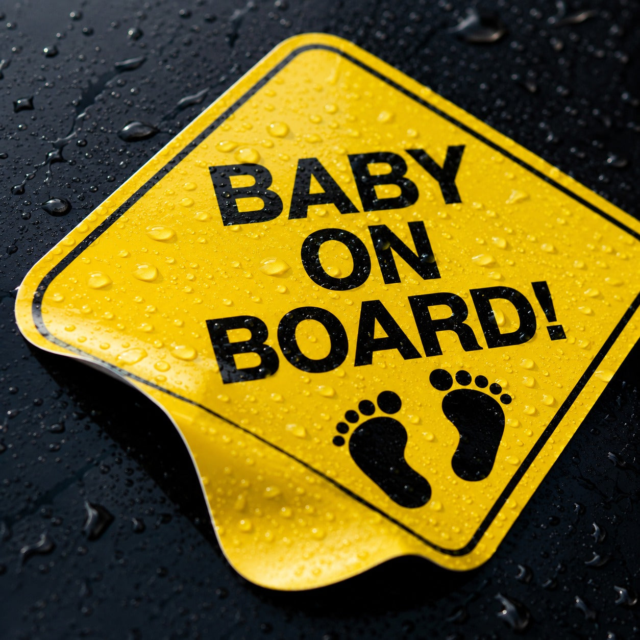 Close-up of a yellow Baby on Board vinyl decal with water beading on the glossy surface.